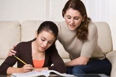 A mother is helping her young daughter with her homework.  They are looking away from the camera.  Horizontally framed shot.